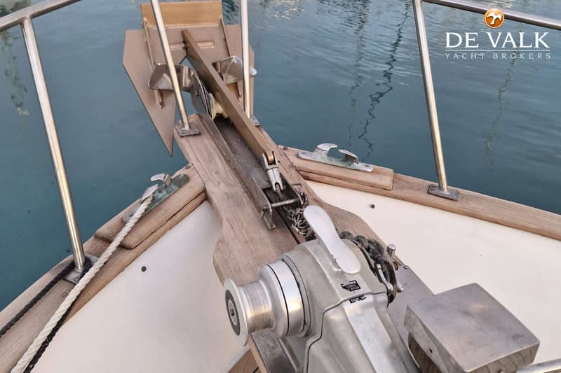 De foto toont de boeg van een boot met een ankerlier, anker en reling, met water op de achtergrond.