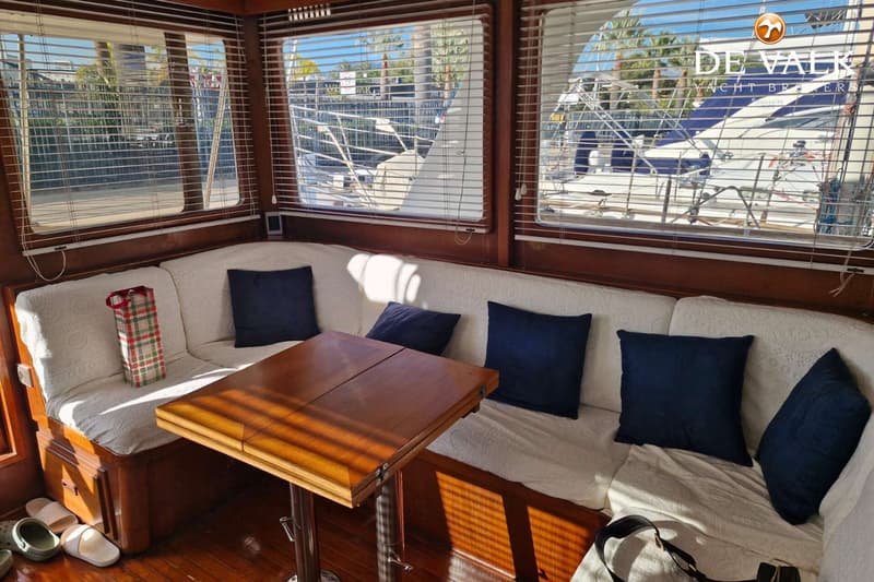 Een interieur van een boot met houten wanden, een U-vormige bank met witte kussens en donkerblauwe sierkussens, en een…