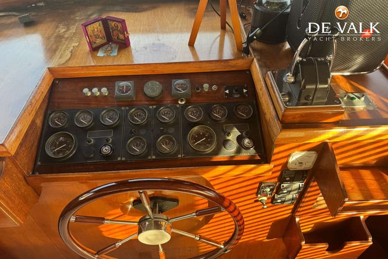 Een houten stuurwiel en een dashboard met diverse meters en schakelaars zijn zichtbaar in een bootinterieur.
