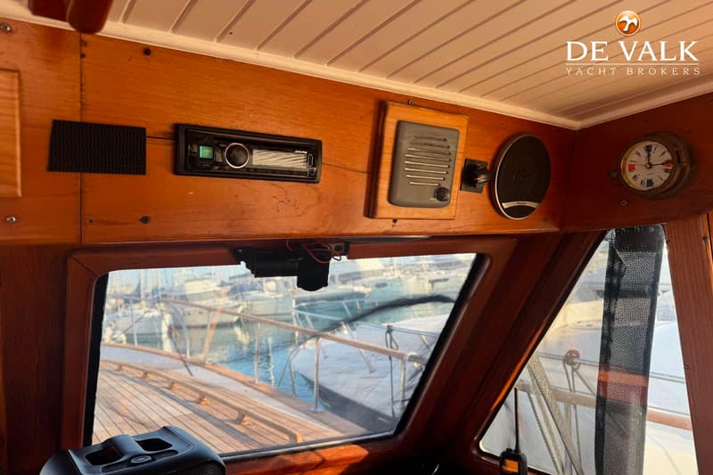 Een houten interieur met een radio, luidspreker, klok en uitzicht op andere boten in een haven.