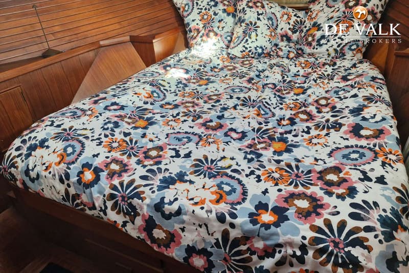 Een bed met een wit dekbedovertrek en kussens met een kleurrijk bloemenpatroon, omringd door houten panelen.