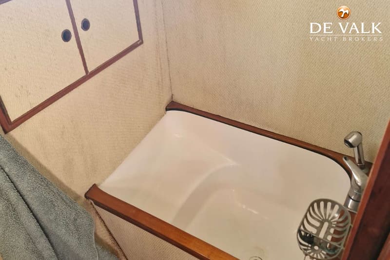 Een witte wasbak met houten randen, een kraan en een zeepbakje zijn zichtbaar in een kleine ruimte met crèmekleurige wanden…