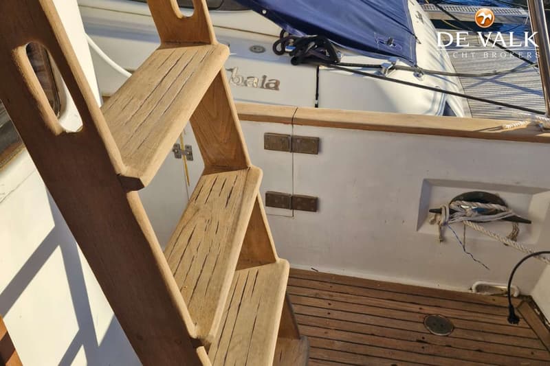 Een houten trap met drie treden leidt naar een dek met houten planken en een witte romp met de naam "bala".