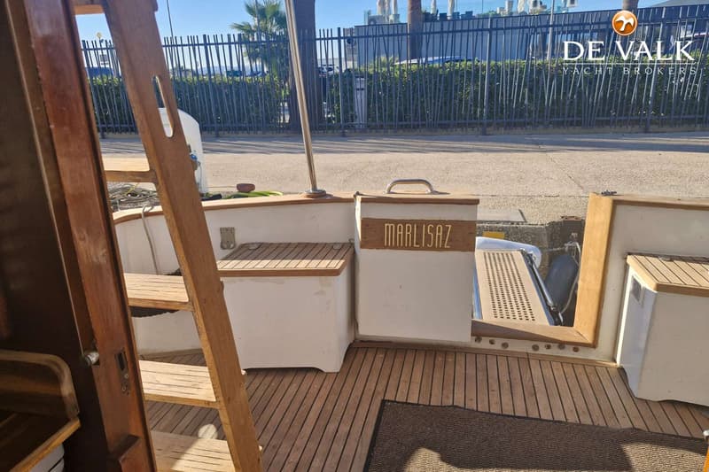 Een houten trap leidt naar een dek met teakhouten vloer, met een opbergbox met de naam "MARLISAZ".