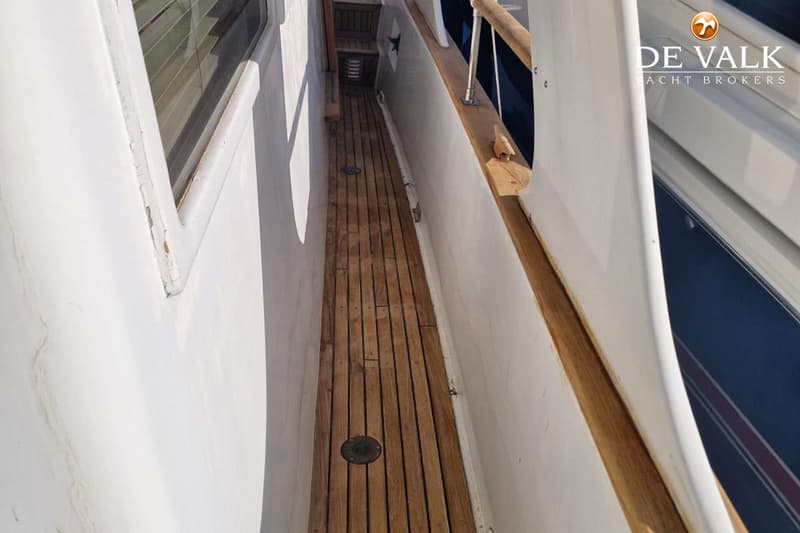 Een houten gangboord met een ronde afvoer en een raam met jaloezieën aan de linkerkant.