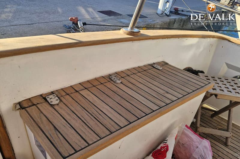 Een houten deksel met drie scharnieren en een houten roosterstoel zijn zichtbaar op het dek van de boot.