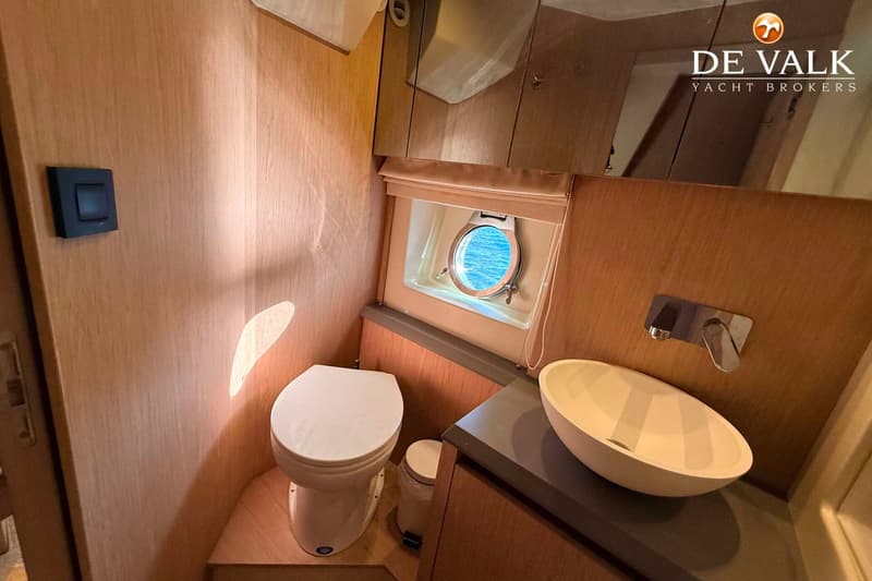 Een toiletruimte met een wit toilet, een ronde wasbak, een patrijspoort en houten wanden.
