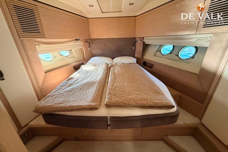 Een kajuit met een tweepersoonsbed, twee patrijspoorten aan elke zijde, en houten kasten en panelen. — Beneteau Monte Carlo 5