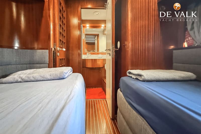 Een interieur van een boot met twee bedden aan weerszijden van een gangpad dat leidt naar een badkamer.