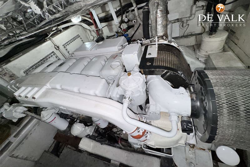 Een witte scheepsmotor met diverse leidingen en filters is zichtbaar in een motorruimte.