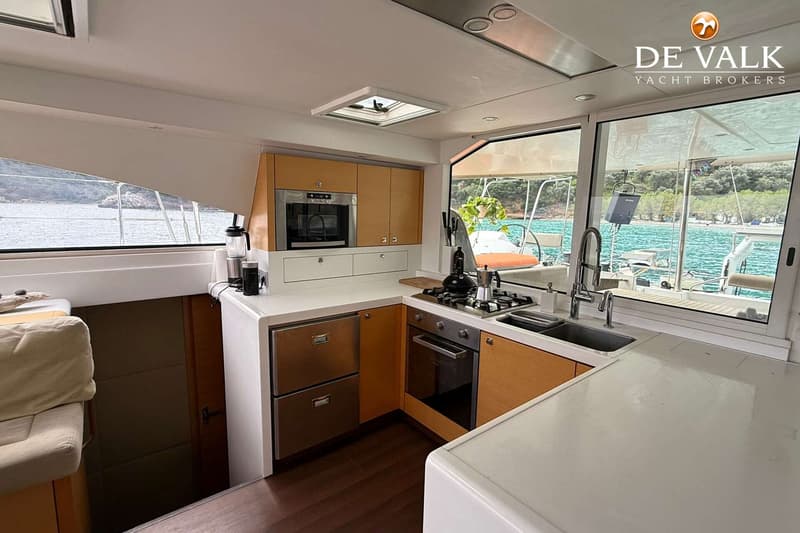 Een bootkeuken met houten kasten, een oven, kookplaat, spoelbak en een raam met uitzicht op water en land.