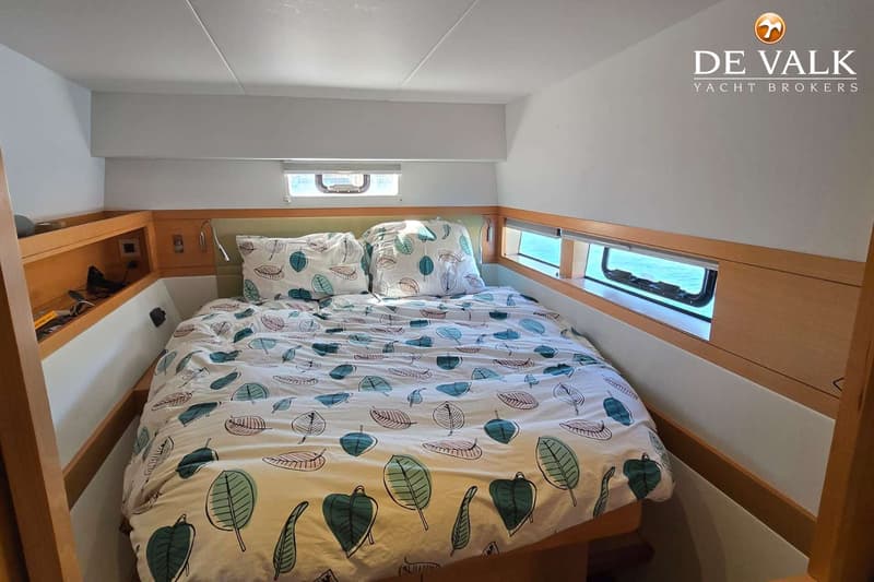 Een slaapkamer met een tweepersoonsbed met een dekbedovertrek met bladmotief, twee kussens en ramen aan beide zijden.