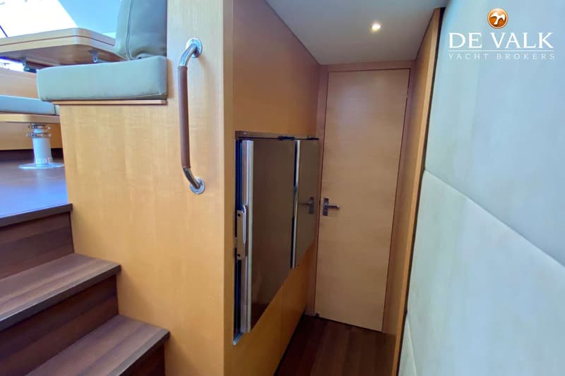Een interieur van een boot met houten traptreden, een leuning, een bankje met kussens en een spiegelende kast.