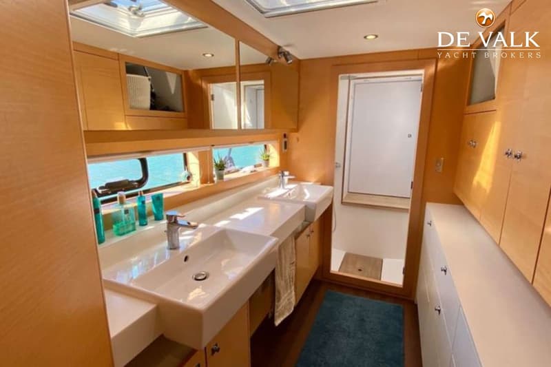 Een badkamer met twee wastafels, een spiegelwand, houten kasten en een deur naar een douchecabine.