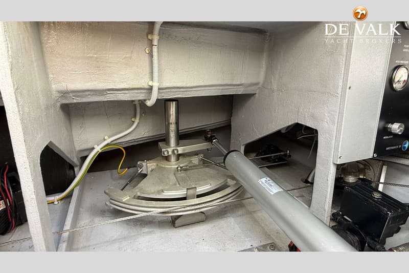 De foto toont een roerinstallatie met een hydraulische cilinder, kabels en een kwadrant in een grijs geverfde ruimte.