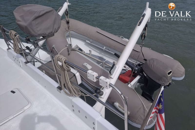 Een grijze bijboot met buitenboordmotor hangt aan davits boven het water, met een Maleisische vlag eronder.