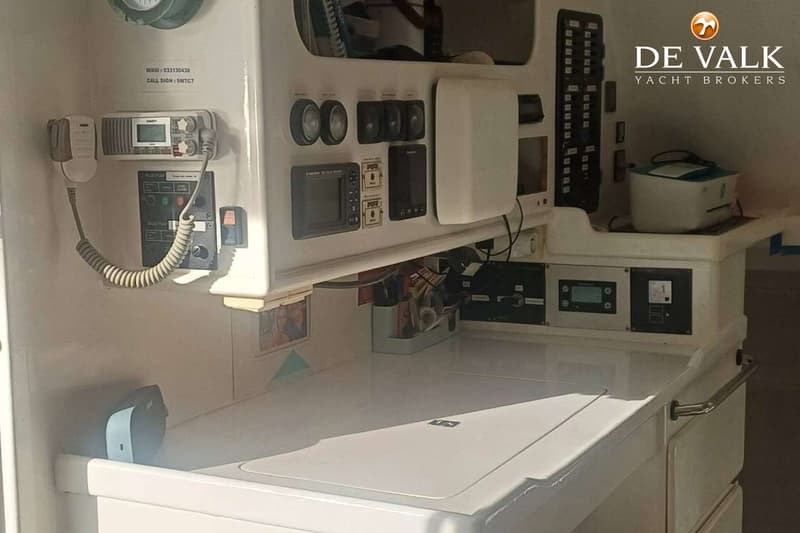 Een witte werkplek met diverse elektronische apparatuur, waaronder een marifoon, meters en een printer.