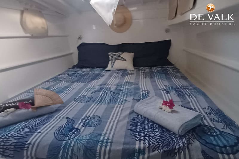 Een slaapkamer met een bed met blauw-wit gestreept beddengoed met zeemotieven, twee donkerblauwe kussens en een kussen met…