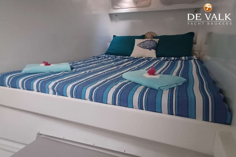 Een bed met blauw-wit gestreept beddengoed, twee turquoise kussens en een kussen met een vis erop.