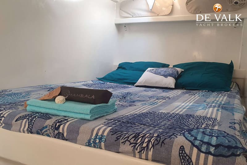 Een bed met blauw-wit gestreept beddengoed met zeemotieven, twee blauwe kussens en een wit kussen met een vis erop.