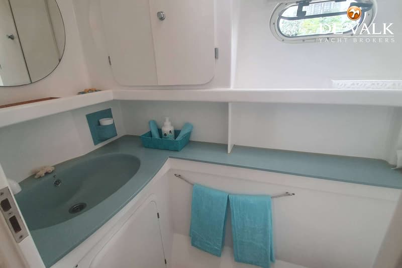 Een badkamer met een wastafel, spiegel, kastjes, een patrijspoort en twee blauwe handdoeken.