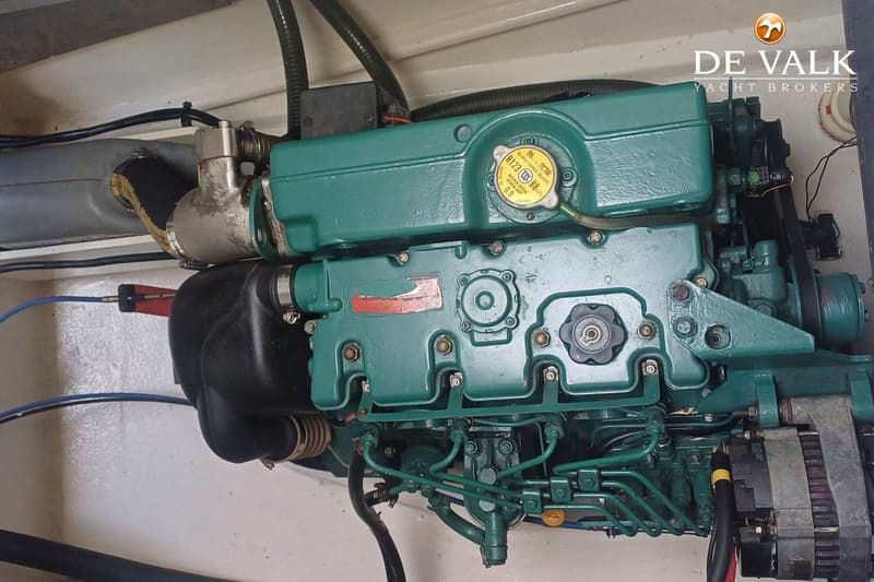 Een detailfoto van een groene scheepsmotor met diverse slangen, kabels en een riem.