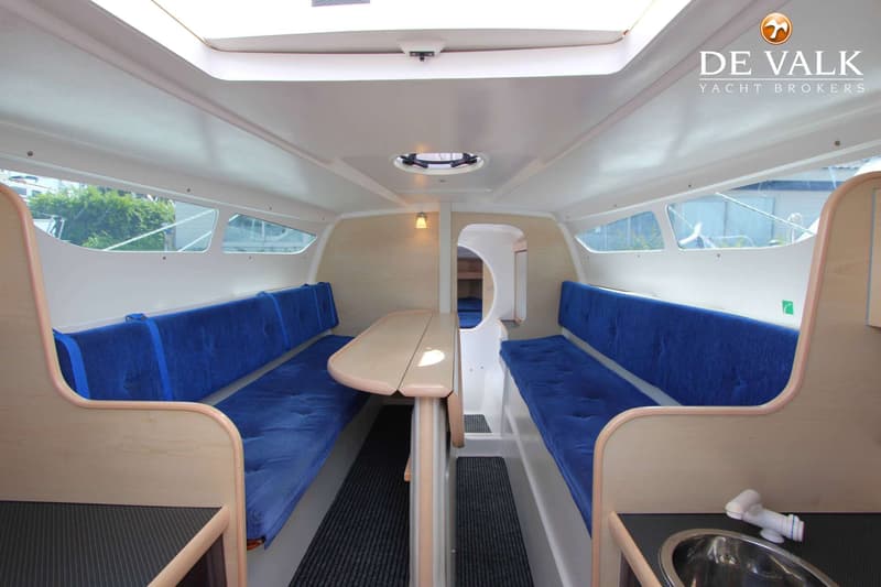 De foto toont het interieur van een boot met blauwe kussens, een houten tafel en een wasbak. — Dragonfly DF 28 Touring