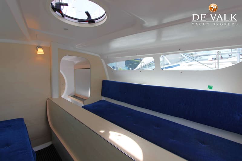 De kajuit heeft blauwe kussens, een patrijspoort, ramen en een lampje aan de wand. — Dragonfly DF 28 Touring