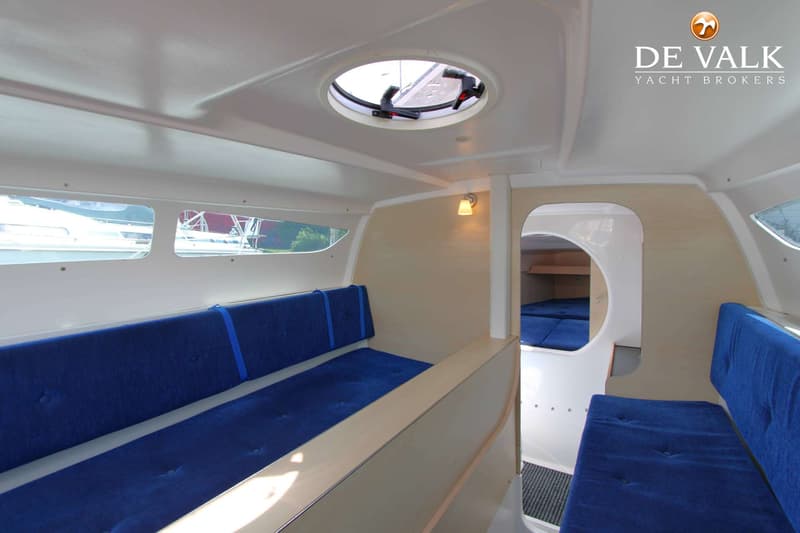 De foto toont het interieur van een boot met blauwe kussens, houten wanden en een rond dakluik. — Dragonfly DF 28 Touring