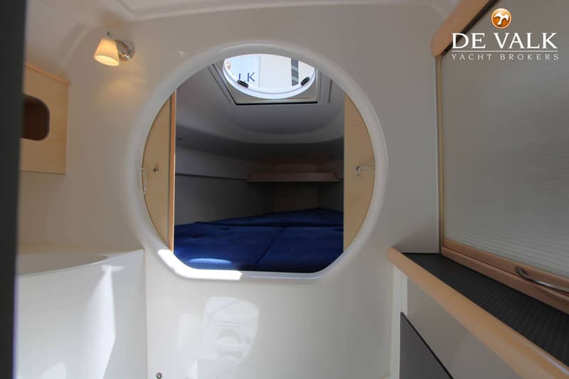 Een interieur van een boot met een doorgang naar een slaapgedeelte met blauwe matrassen en een dakluik.
