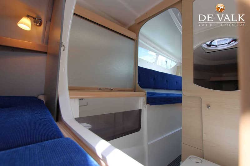 De foto toont het interieur van een boot met blauwe kussens, houten accenten en een leeslampje. — Dragonfly DF 28 Touring