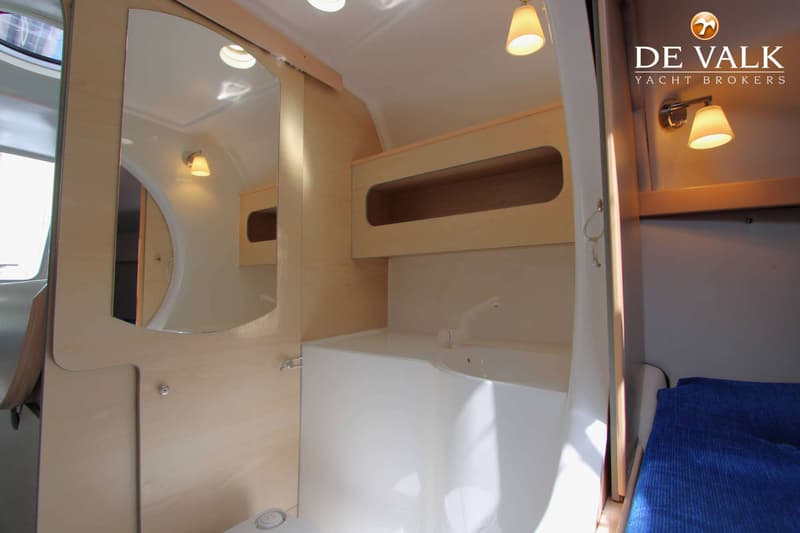 Een badkamer in een boot met een spiegel, wastafel, toilet en een blauw bed aan de rechterkant. — Dragonfly DF 28 Touring