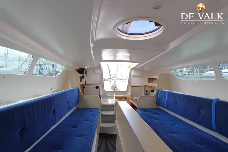De foto toont het interieur van een boot met twee banken met blauwe kussens, een luik en ramen. — Dragonfly DF 28 Touring