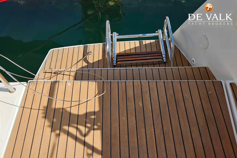 Een teakdek met een zwemtrap en een touw dat in het water ligt, met het logo van De Valk Yacht Brokers rechtsboven.