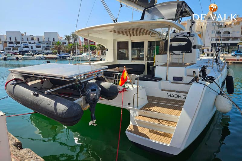 Een witte catamaran met een bijboot en zonnepanelen aan de achterzijde, aangemeerd in een haven.