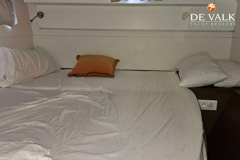 Een kajuit met een bed met wit beddengoed, drie witte kussens en één oranje kussen. — Lagoon 40