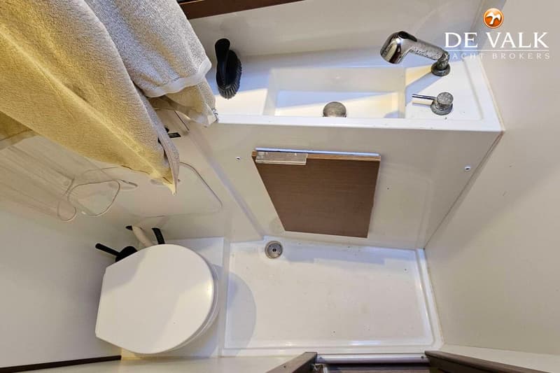 De foto toont een compacte badkamer met een toilet, wastafel met kraan en douchekop, en een afvoer in de vloer.