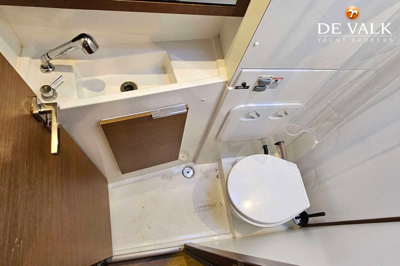 Een witte badkamer met een wastafel, douchekop, toilet en een houten kastje.