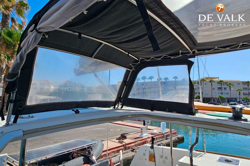 De foto toont een deel van een boot met een zwarte bimini en doorzichtige zijpanelen, met uitzicht op een haven en gebouwen.