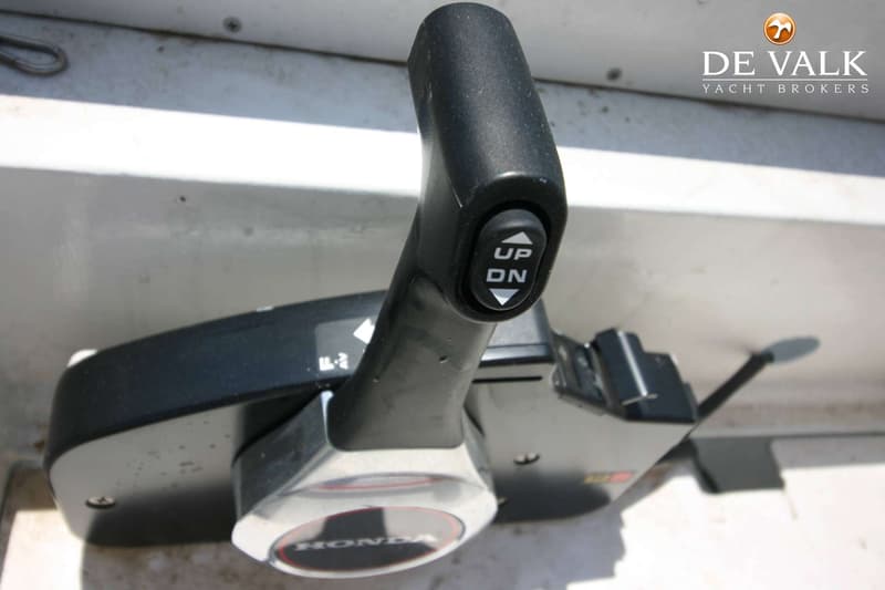 Een close-up van een zwarte Honda gashendel met een "UP/DN" knop, gemonteerd op een lichtgrijze ondergrond.