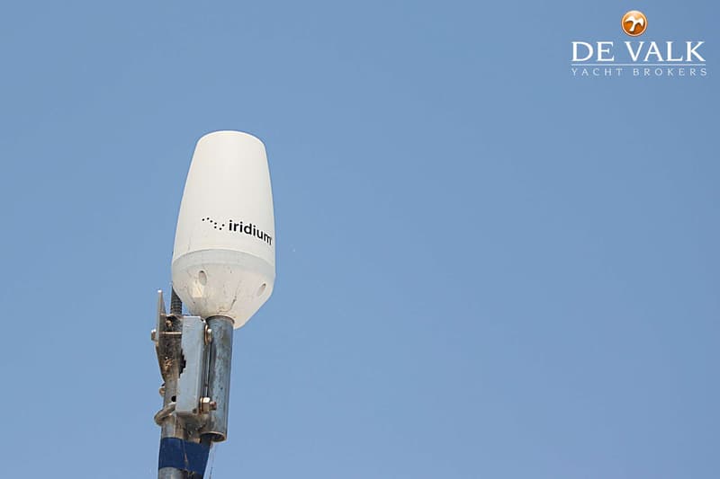 Een witte Iridium satellietantenne is gemonteerd op een metalen paal tegen een helderblauwe lucht.