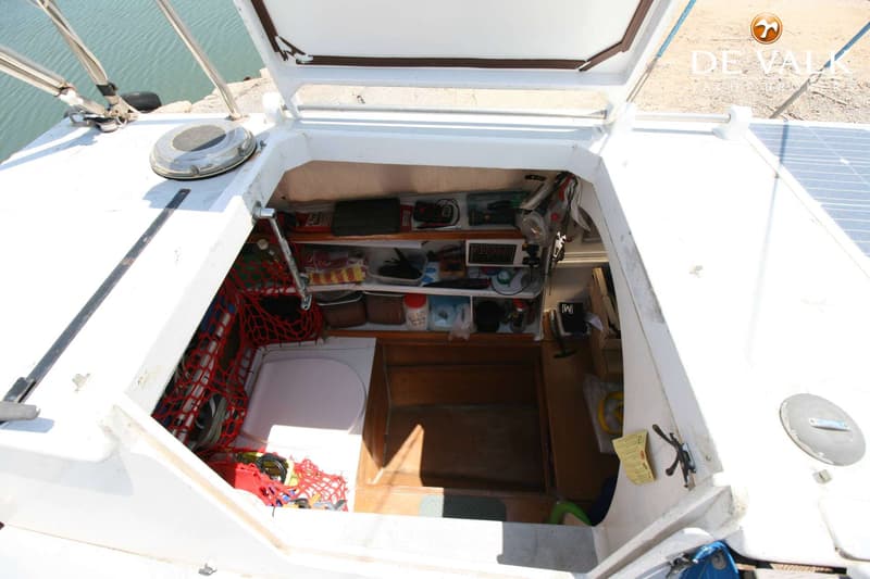 Een open luik van een boot toont een rommelige kajuit met planken vol spullen en een toilet. — Wharram Tiki 30