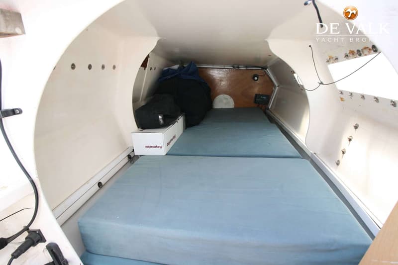 De foto toont het interieur van een boot met twee blauwe matrassen, een witte Raymarine doos en een zwarte tas.