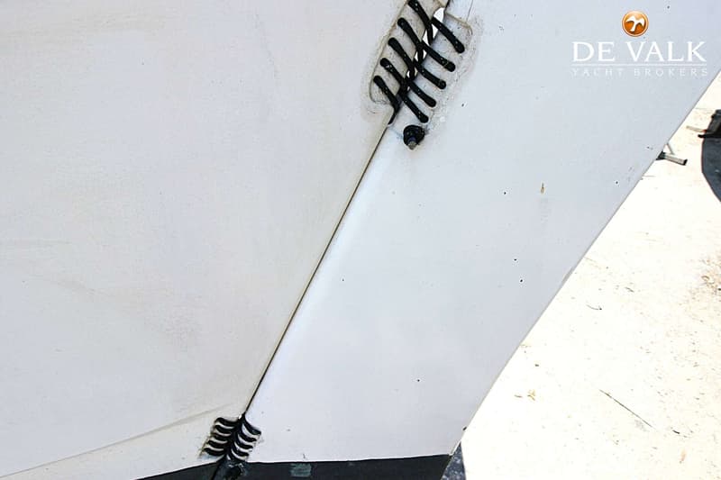 De foto toont een detail van een witte bootromp met een zwarte, vlechtachtige verbinding en het logo van De Valk Yacht…
