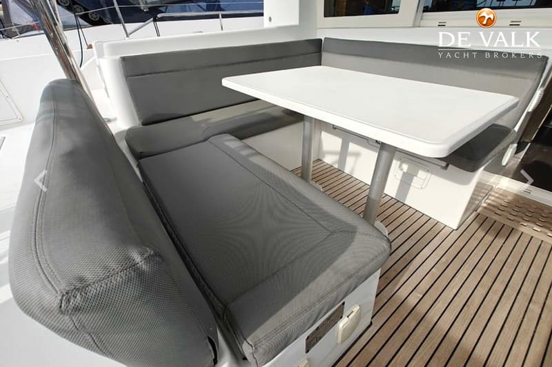 Een bootinterieur met een witte tafel, grijze kussens op banken en een houten vloer.