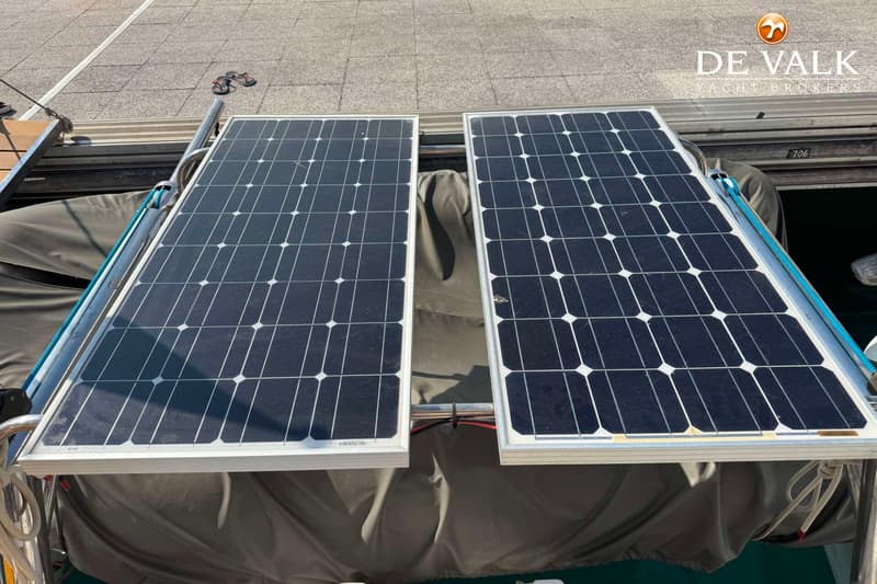 Twee zonnepanelen zijn gemonteerd op een boot, met een grijs dekzeil eronder en een grijze kade op de achtergrond.