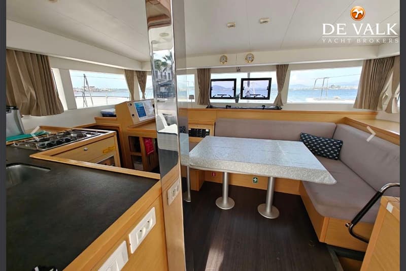 De foto toont het interieur van een boot met een kombuis, een eethoek met banken en een tafel, en ramen met uitzicht op…