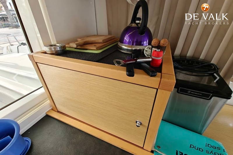 Een houten kastje met een paarse fluitketel, snijplanken, walnoten, een flesopener en een ijsblokjesmachine erop.