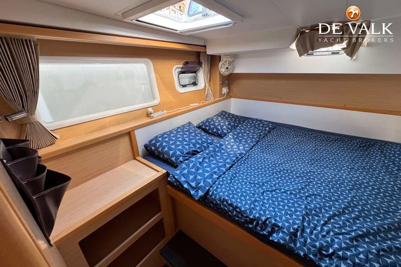 Een kajuit met een tweepersoonsbed met blauw beddengoed, houten wanden, ramen en een dakluik. — Lagoon 39
