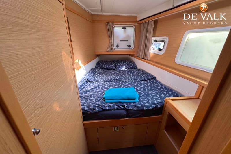 Een kajuit met een tweepersoonsbed met donkerblauw beddengoed, twee ramen en houten wanden. — Lagoon 39